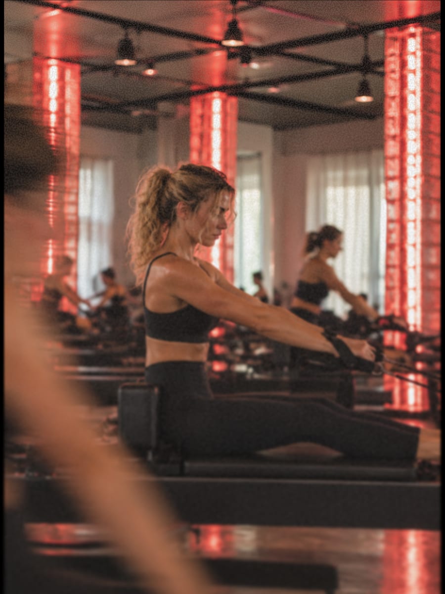Une pratiquante assise sur un Reformer, bras tendus sur les sangles, de profil.