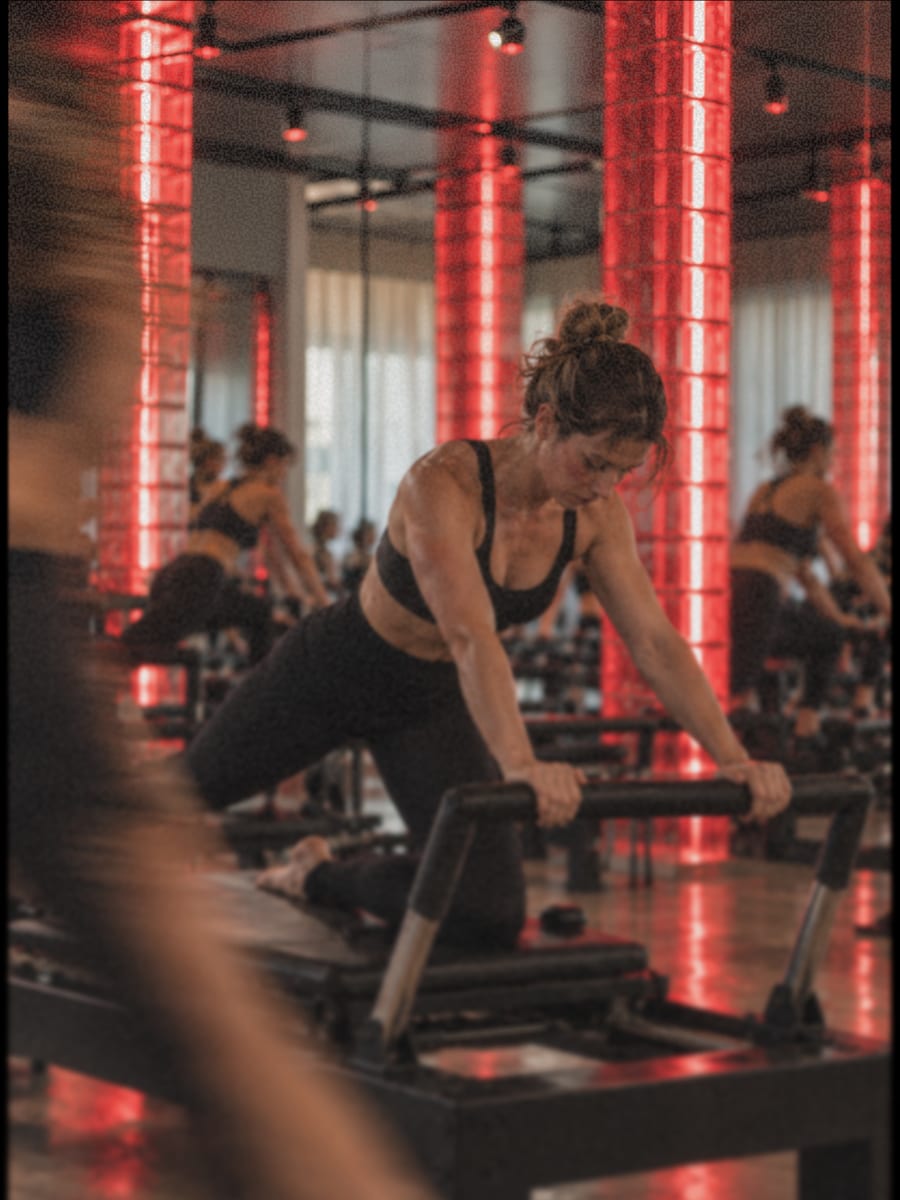 Une pratiquante à genoux sur un Reformer, mains sur la barre, avant la première répétition.