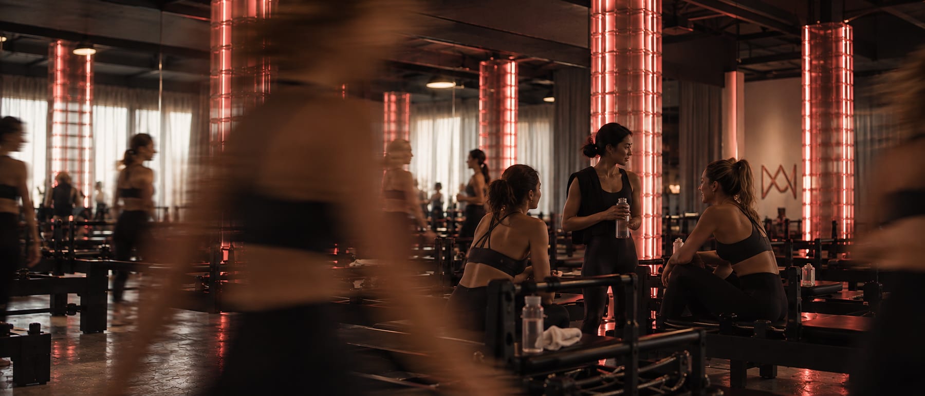 Des membres de Studio MA réunis entre deux cours dans la salle Reformer, sous la lumière rouge des colonnes.